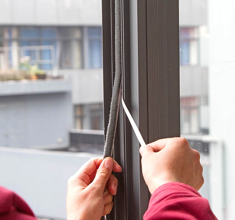 Self-adhesive weatherstrip being applied along a window frame